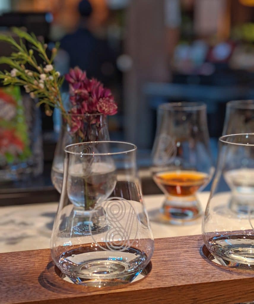 Image of tasting glasses with a vase of flowers in the background.