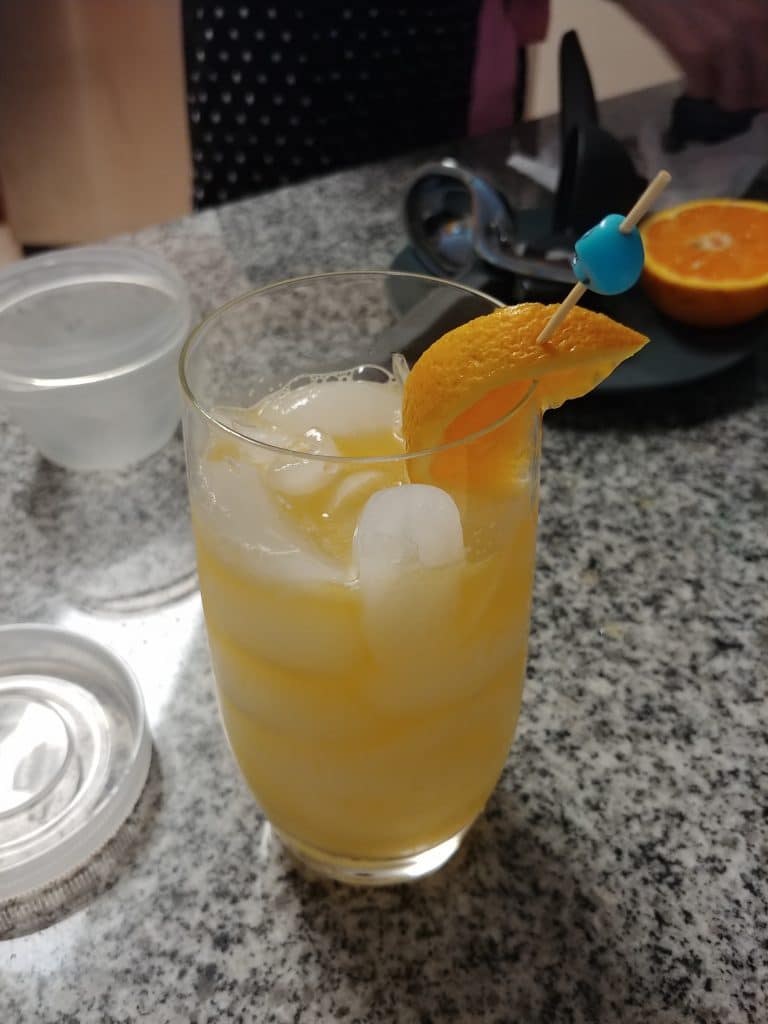 orange drink with ice in a pint glass with an orange wedge as a garnish