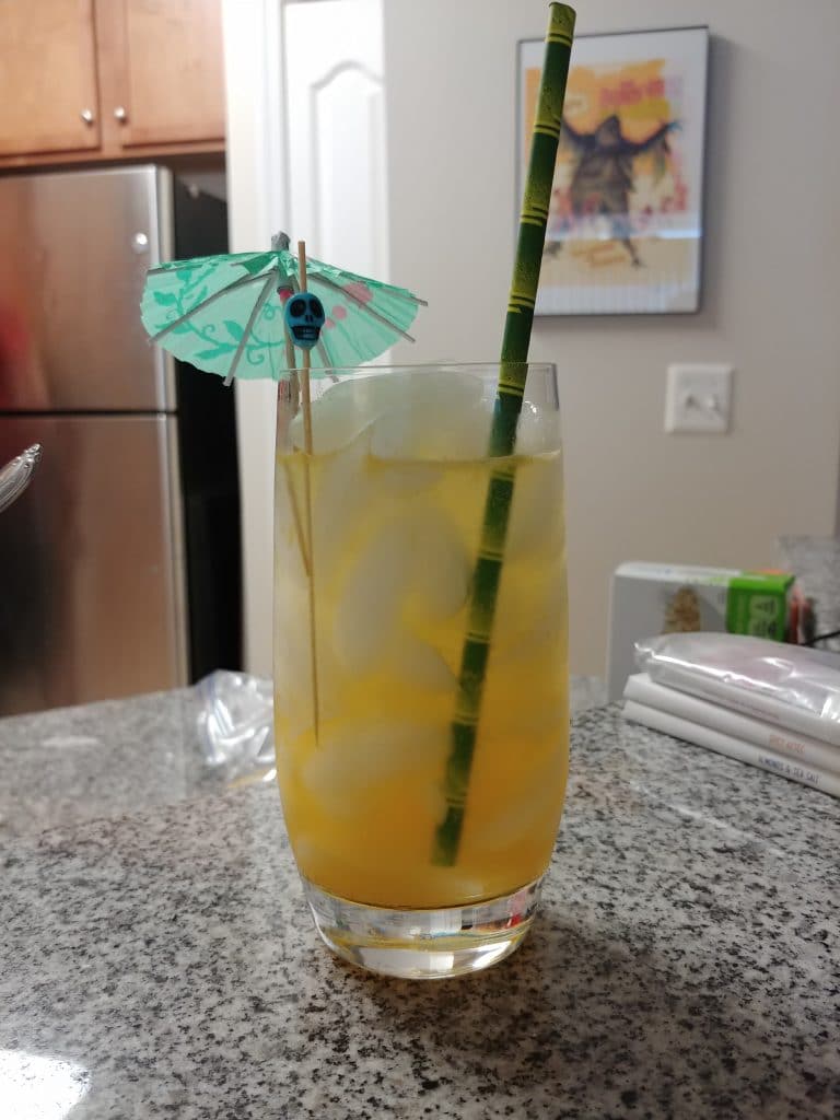 Tall glass of an orange liquid with a straw and tiki accessories