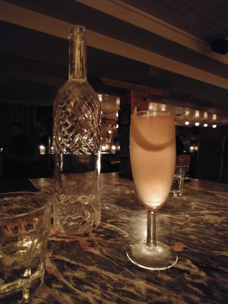 Cocktail in a flute with a fancy glass bottle of water behind it at a bar table